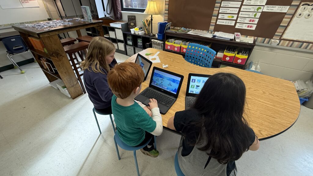 Three young students on laptops learn curriculum in an elementary school class room